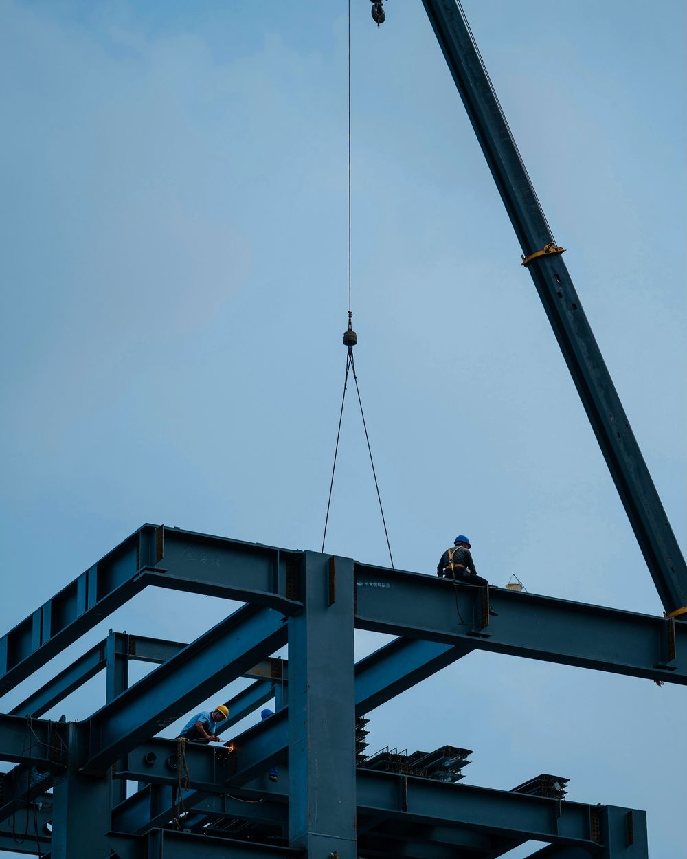 Kran hebt einen Stahlträger an ein Stahltragwerk, Monteure auf der Konstruktion (Beispielfoto)