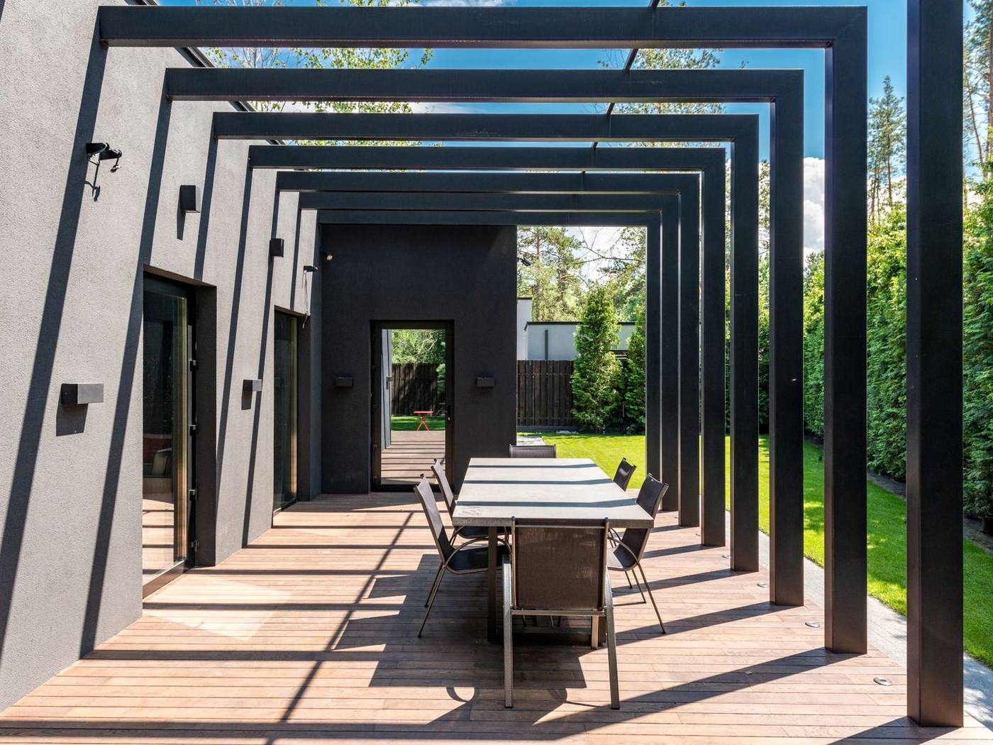 Mehrteilige Pergola aus dunklem Stahl über einer Terrasse mit Esstisch